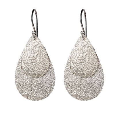 Queen Pear er et sæt flotte øreringe i sort sterlingsølv med flade vedhæng i let banket overflade, der giver øreringene en flot struktur og en rå kant. Øreringene er lette at bære og er perfekt til en aften i byen, eller hvis hverdags-outfittet skal pifte